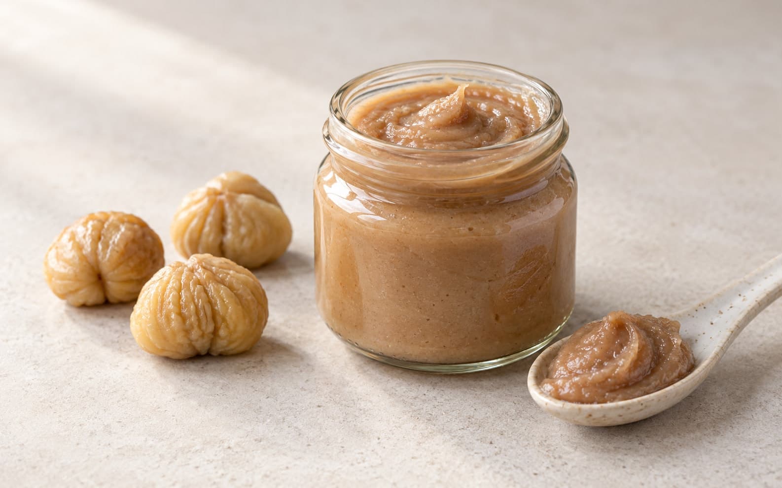 Tarro de cristal con crema de castañas, una cuchara de cerámica con crema y tres castañas peladas